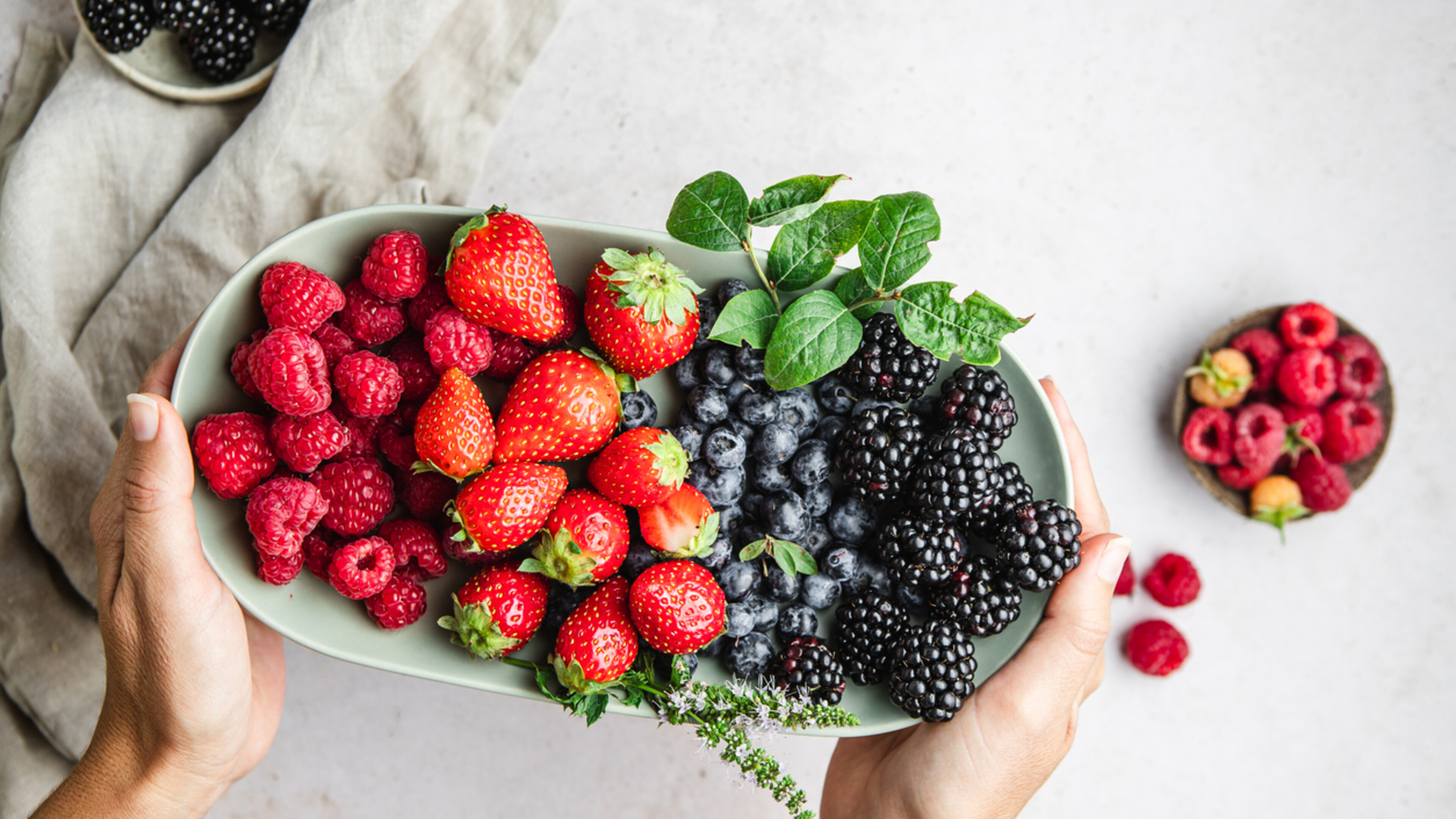close up of hands holding a bowl of various berries over a white surface