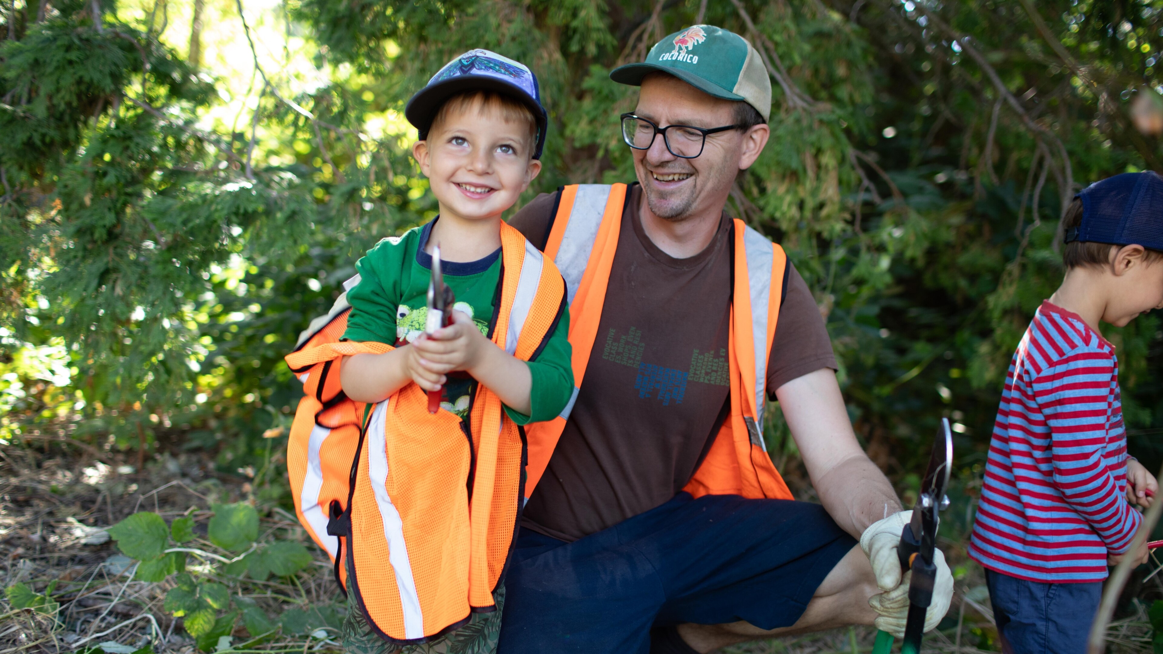 young boy and dad wearing orange vest and working on a park clean up