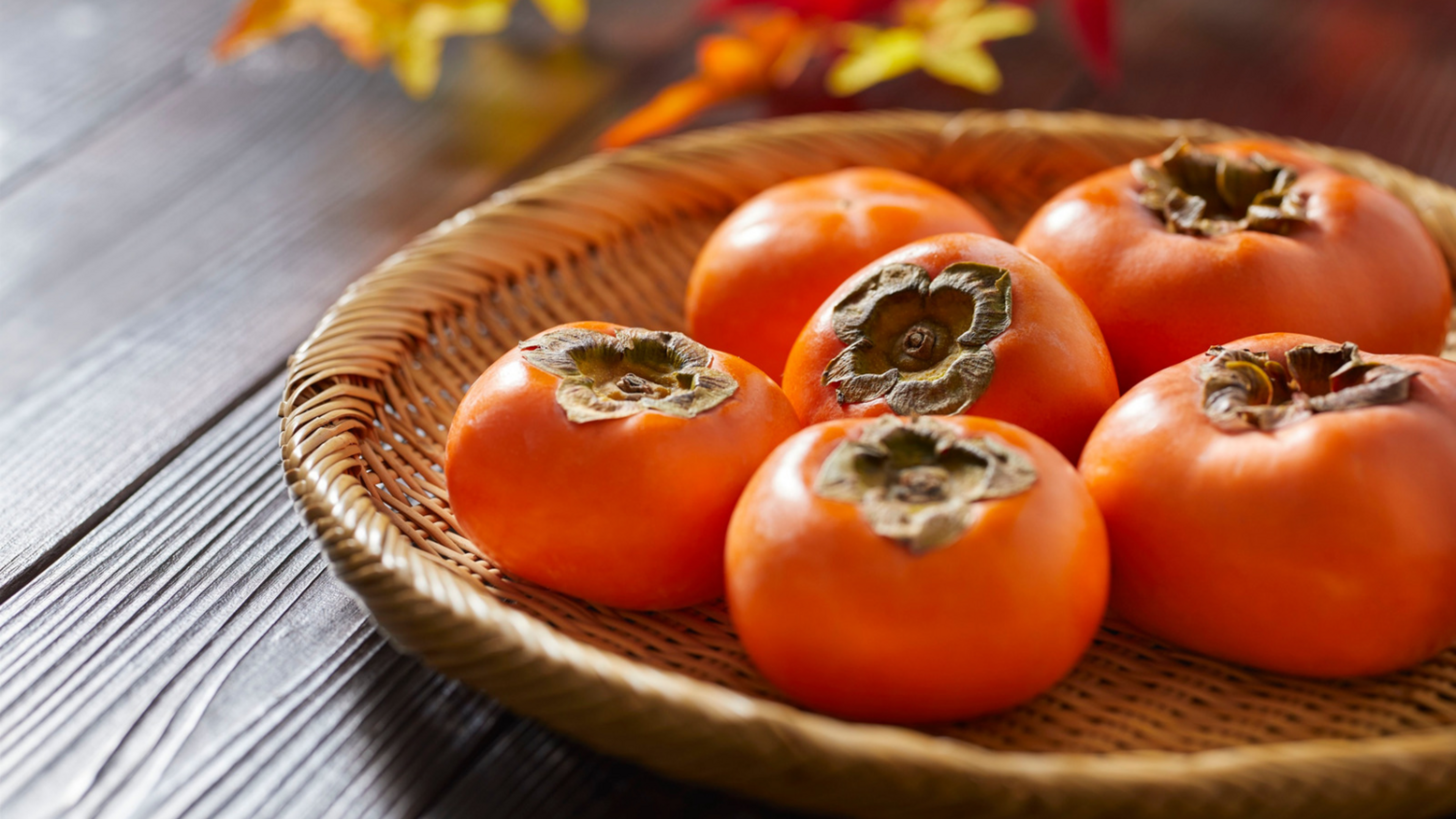 persimmons in a bowl with leaves in the background