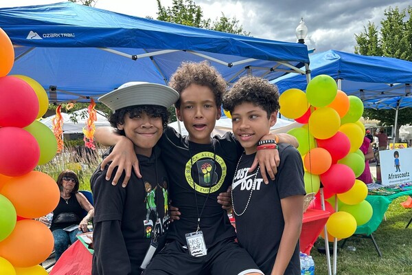 two boys holding up another boy between them with balloons in the background