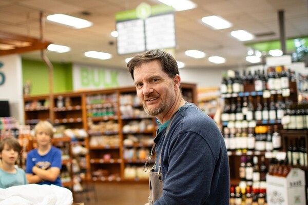 man in apron lifting a box in the produce department of a grocery store