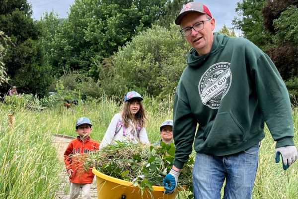 man in a green sweatshirt and hat pulling a wagon full of yard waste