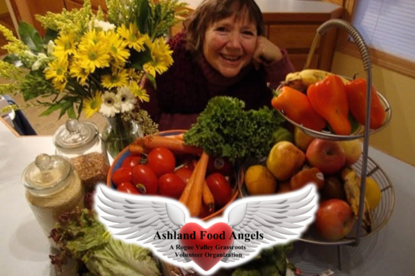 woman behind fresh fruits and vegetables with ashland food angels logo