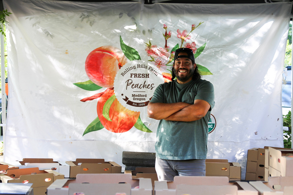 Produce Manager, Joe stands with arms crossed and smiling in his Peach Pop-Up Tent.