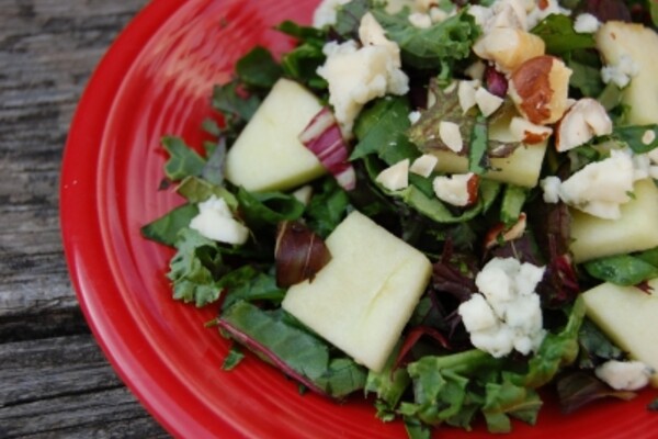 mixed green salad with honeycrisp apples hazelnuts and blue cheese on a red plate