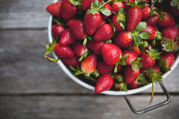 strawberries in a colander on a wood surface