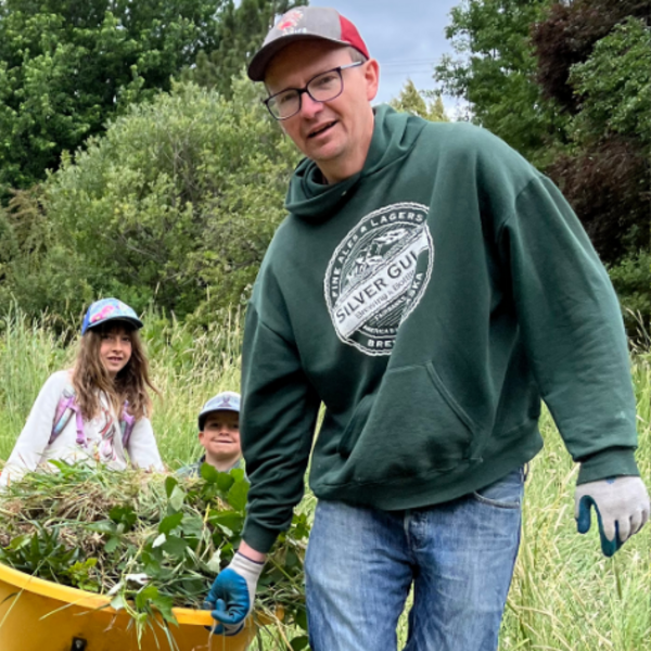 man in a green sweatshirt and hat pulling a wagon full of yard waste