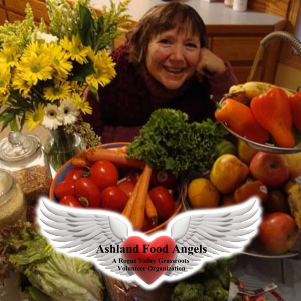 woman behind fresh fruits and vegetables with ashland food angels logo