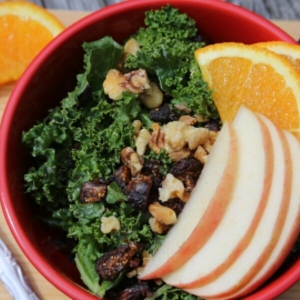 kale salad with apples and oranges in a red bowl