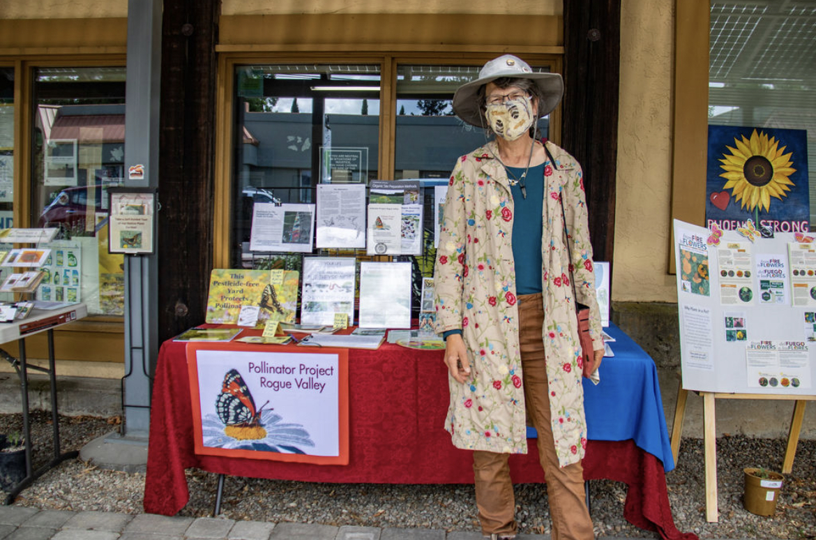Photo Credit: Chelsea Whitney Art a representative from Pollinator Project Rogue Valley stands in a flower print jacket in front of an informational table