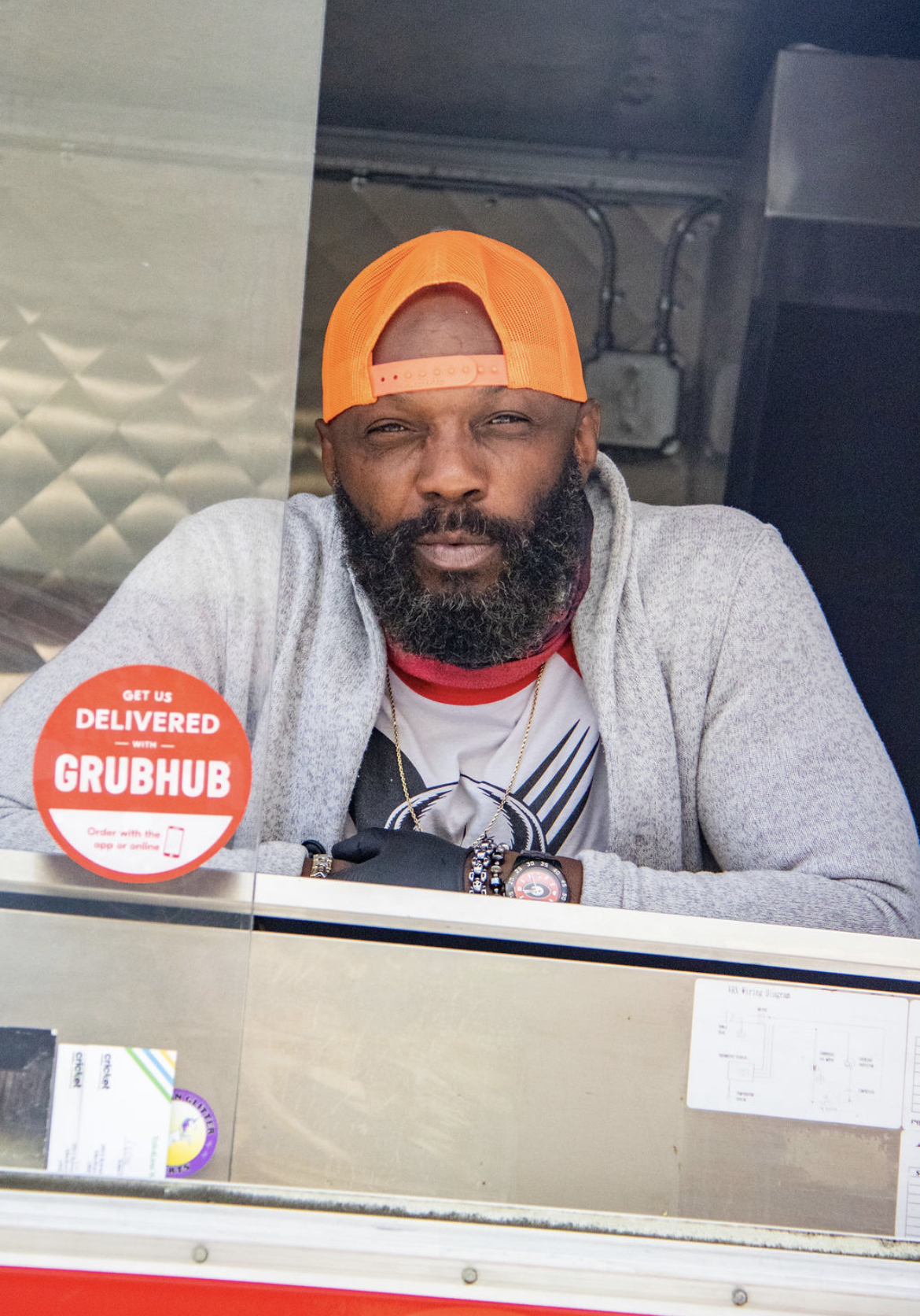 Photo Credit: Chelsea Whitney Art a man in a backwards orange cap looks on from the counter of his red food truck